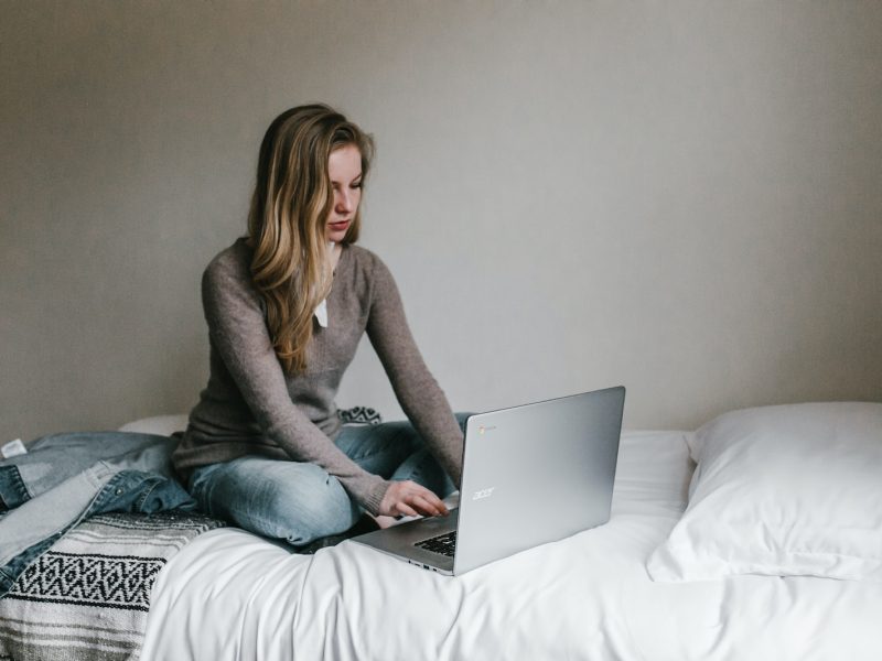 woman typing on MacBook Pro while sitting on bed in room